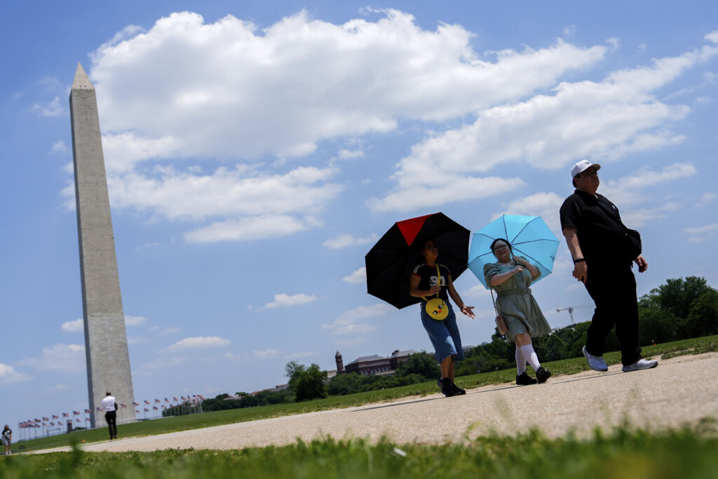 People using umbrellas to shield themselves from the sun as they walk along the National Mall.