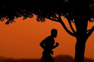 A man is silhouetted against the sky at sunset as he jogs in a park