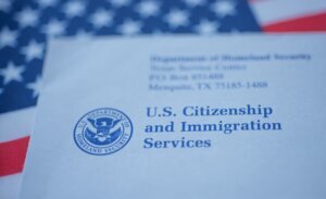 Hand touching Letter (Envelope) from USCIS on flag of USA background.