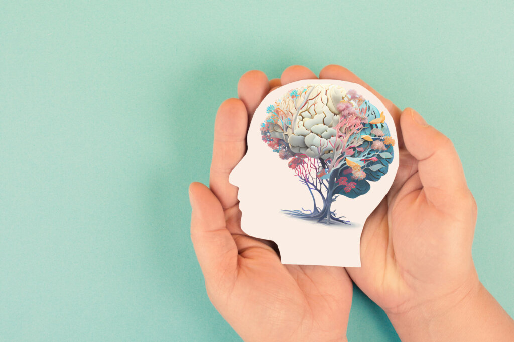 Hands holding paper head, human brain with flowers, self care and mental health concept