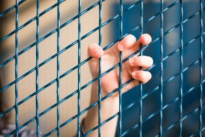 A child's hand hooked on a blue metal fence