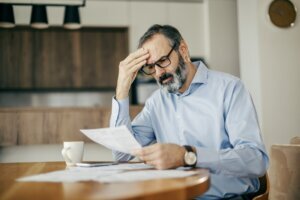 Worried man calculating bills and struggling with financial stress at home