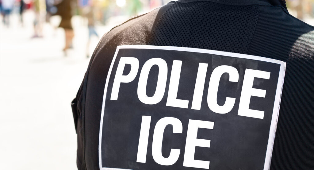 Ice Police Immigration and Customs Enforcement Close up of POLICE ICE marking on the back of a hi visibility stab proof vest worn by a police officer at the scene of an incident.