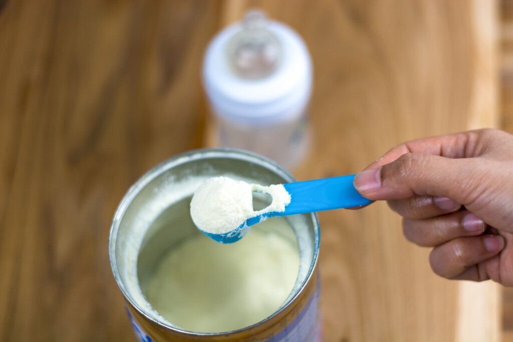 New parents Powder milk and blue spoon on light background close up. Milk powder for baby in measuring spoon on can. Powdered milk with spoon for baby. Baby Milk Formula and Baby Bottles.