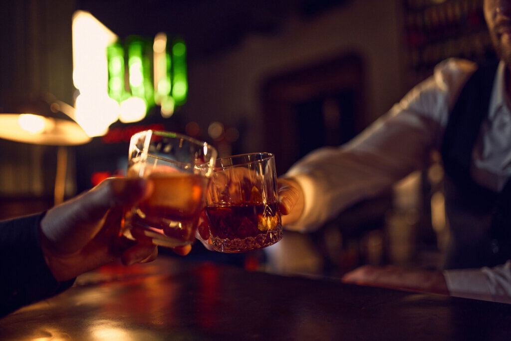 Hands clicking whiskey glasses in warm bar light